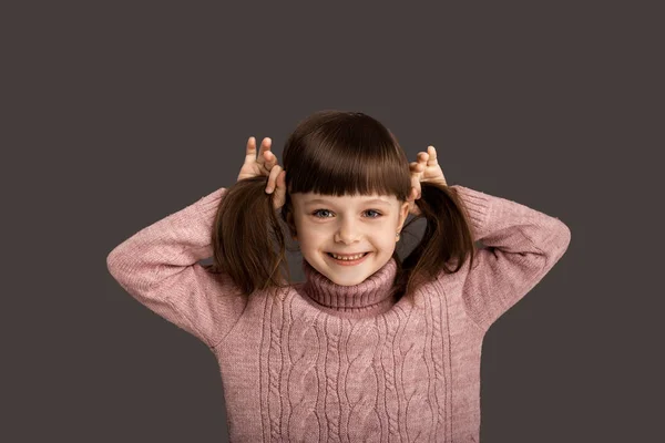 健康强壮的头发 一个小女孩把她的马尾辫放在饼干里 对着摄像机笑 她喜欢她的新发型 就像她在孩子们的理发店里那样 — 图库照片