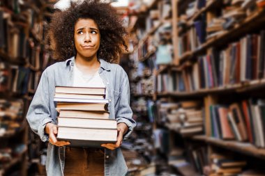 Elinde ağır bir kitap yığını, genç bir kız, Afro-Amerikan bir öğrenci, üniversitedeki görevleri konusunda şaşkın ve mutsuz görünüyor. Kütüphanede kitaplıkların arkaplanının karşısında durur 