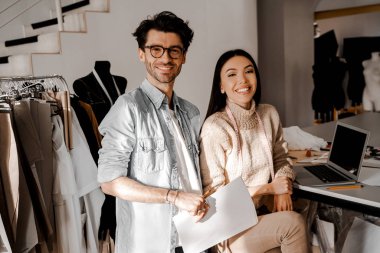 Mutlu gülümseyen tasarımcılar kameraya bakan terzilik kurslarının tasarımcıları, mesleki becerilerini göstermeye hazırlar, terzilik stüdyosunda bir gün planlıyorlar. Yeni müşteriler bekliyor. Çalışmaya hazır