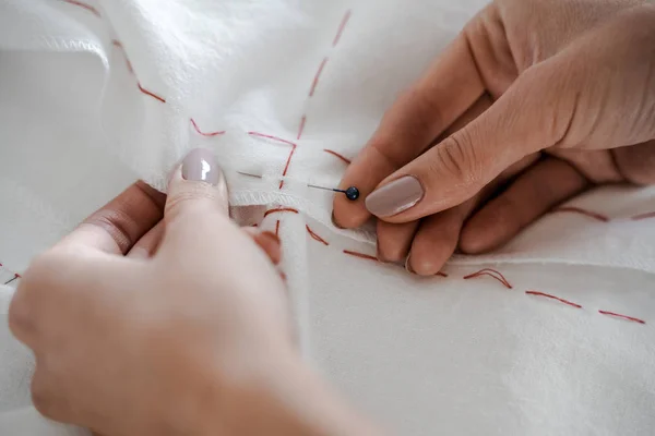 Tailor professional detail, sewing and tailoring concept, tailor woman with thread in needle stitching fabric. Hands sewing with a needle and thread. Fingers pulling thread into the needle