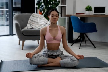 Gülümseyen çekici bir kadın yoga yapıyor Ardha Padmasana egzersizi yapıyor, Yarım Lotus pozunda meditasyon yapıyor spor kıyafetleri giyiyor. Sağlıklı insan yaşam tarzı, güçlü kadın vücudu.