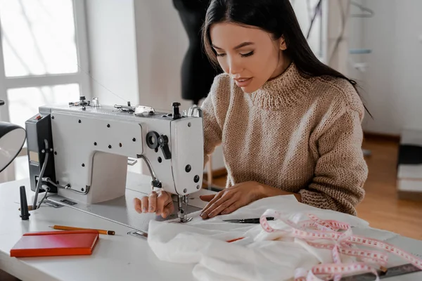 Odaklanmış güzel Asyalı kadın dikiş makinesinde dikiş dikiyor, en sevdiği iş. Yaratıcı gelişim sürecinde dikiş, tasarım stüdyosu, terzi, tasarımcı kıyafeti, manufactory.
