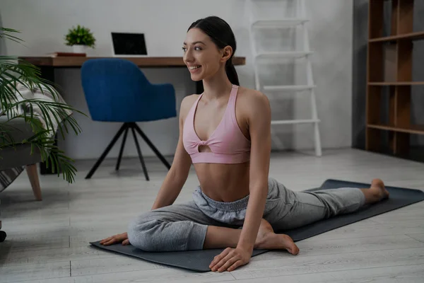 Beautiful athletic strong woman, a trainer trains and does sports in the morning at her home, on a sports mat, does yoga and smiles happy. Healthy lifestyle concept
