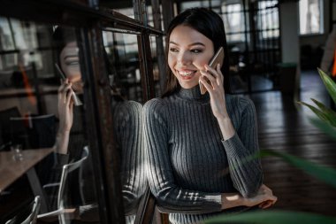 Gülümseyen güzel bir ofis çalışanı meslektaşlarıyla cep telefonuyla konuşuyor. Başarılı iş stratejisi konsepti. İş yerinde kendine güvenen bir ofis çalışanı. İnsan yaşam tarzı