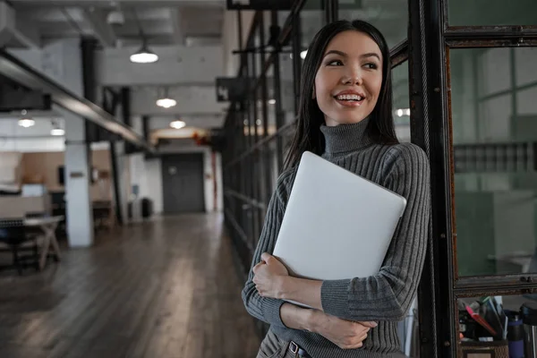 Beautiful smiling asian woman work in modern office, holding laptop, have free time break. Successful business strategy plan concept. Confident office worker indoor, coworking space. People lifestyle