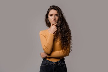 Gri arka planda uzun kıvırcık saçlı, sarı giyimli yaratıcı bir insan. Ne unuttuğunu hatırlamaya çalışıyorum. Düşünceli duruş ve yüzünde duygu.