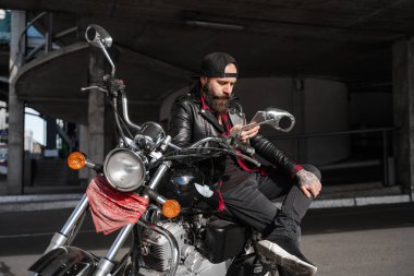 Motosikletli acımasız sakallı adam, siyahlar içinde oturan, motosiklet stili, cep telefonu ve internet teknolojileri kullanan şık adam, 5G bağlantısı ile iletişim.. 