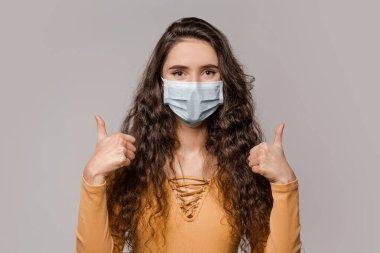 Dur dedim! Covid-19 kuralları, maske rejimi. Mesafeyi karantinada tutmak, dünya salgını, grip salgını. Tıbbi maske takan genç ve güzel bir kadın her şeyin yolunda olduğunu gösteren bir jest gösteriyor.