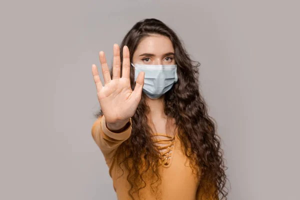 Dur dedim! Covid-19 kuralları, maske rejimi. Mesafeyi karantinada tutmak, dünya salgını, grip salgını. Kadın yüzüne tıbbi bir maske takmış ve elini kullanarak hareket talebini işaret etmiş.