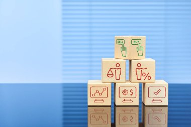 Görsel iş konsepti, alıp satmayı seçmek. Yüzeyinde yansıması olan bir piramide yerleştirilmiş altı tahta küp. Bloklara çeşitli eylem simgeleri yerleştirildi. Metin için boş alan.