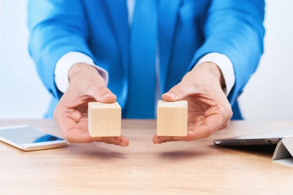 ビジネスマンはそれぞれの手でテーブルの上に木製の立方体を保持します または碑文のブロックには空き領域があります インフォグラフィックのレイアウト — ストック写真