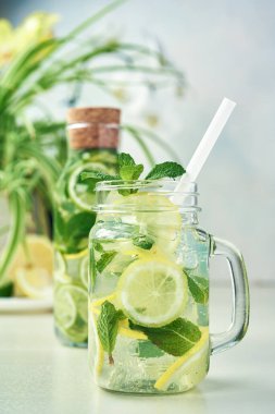 Bir bardak ve bir şişe ev yapımı limonata, limon ve nane tezgahından yapılmış ahşap yemek masasında. Soğuk, ferahlatıcı yaz limonatası ya da mojito..