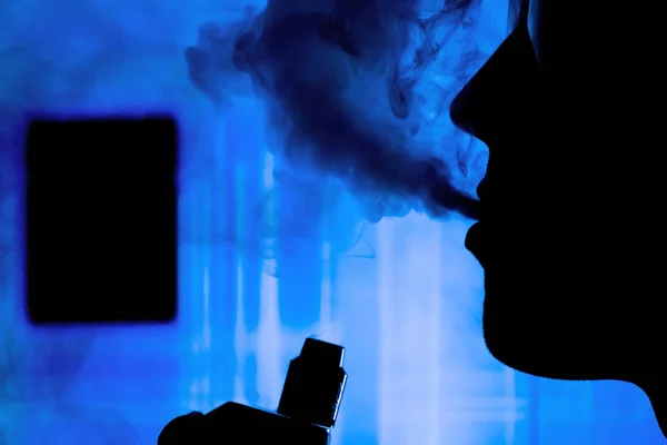 Man with electronic cigarette and smoke vapping with neon lights background — Stock Photo, Image