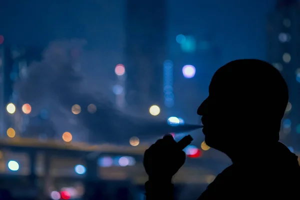 Man med elektronisk cigarett och rök vapping med staden bokrh ljus bakgrund Stockbild