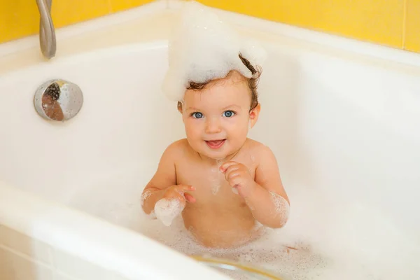 Smiling kid with foam and soap bubbles in bathroom.