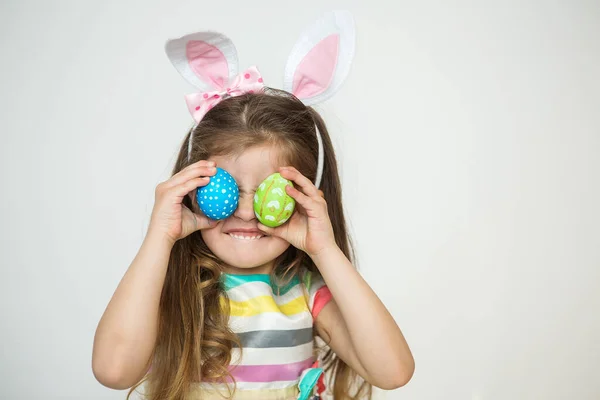 Menina bonito vestindo orelhas de coelho e segurando pintado ovos de Páscoa e sorrindo em um fundo branco. Dia de Páscoa . — Fotografia de Stock