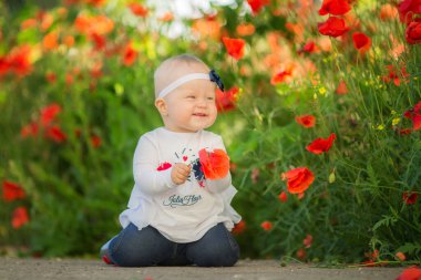 Güzel küçük bir kızın portresi Baharda kırmızı gelincik çiçekleri arasında eğleniyor.