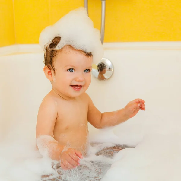 Smiling kid with foam and soap bubbles in bathroom.