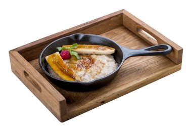 Beyaz arka planda bir tavada kahvaltı. Muz ve şuruplu yulaf ezmesi. Tahta tepside.