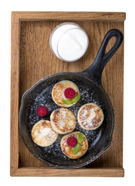 Beyaz arka planda bir tavada kahvaltı. Ahududu ve ekşi kremalı peynirli kek. Tahta tepside.