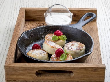 Beyaz arka planda bir tavada kahvaltı. Ahududu ve ekşi kremalı peynirli kek. Tahta tepside.