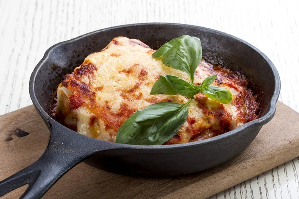 Lasagne in een gietijzeren pan op een houten plank. Traditioneel Italiaans gerecht — Stockfoto