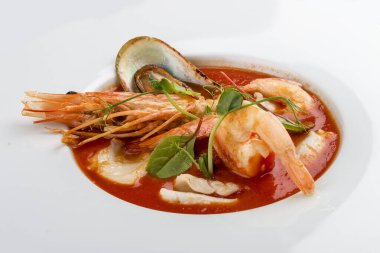 Fransız balık çorbası, karides, midye ve deniz tarağı. Tekstil arka planında beyaz bir tabakta