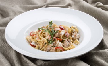 Tavşan ve biberli, beyaz tabakta krema soslu Tagliatelle. Tekstil arka planı