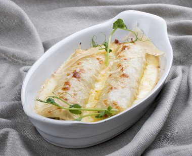 Beyaz seramik tabakta pişirilmiş kıymalı Cannelloni. Tekstil arka planı