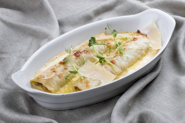 Beyaz seramik tabakta pişirilmiş kıymalı Cannelloni. Tekstil arka planı