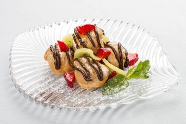 Tatlı profiteroller, kremalı, çilekli ve kivili dilimli.