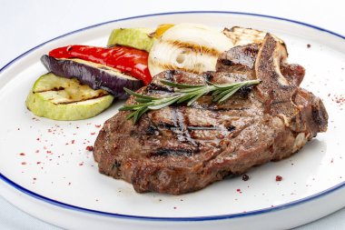 Beyaz arka planda ızgara sebzeli dana kemiği bifteği.