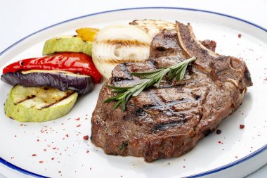 Beyaz arka planda ızgara sebzeli dana kemiği bifteği.