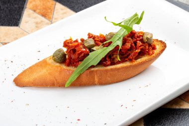 Beyaz bir tabakta fırında biber ve kapari.