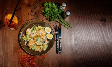 Tahta masadaki siyah tabakta Sezar salatası. Eski ahşap masada taze sezar salatası.