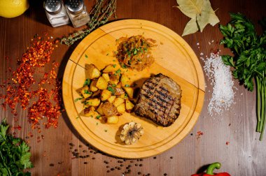 Tabakta et ve kızarmış patatesle ahşap bir masada yemek.