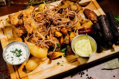 Bira ve abur cubur seçimi. Cips, balık, bira sosu. Masanın üzerinde soslu, koyu arkaplanda bir sürü farklı bira aperatifi.