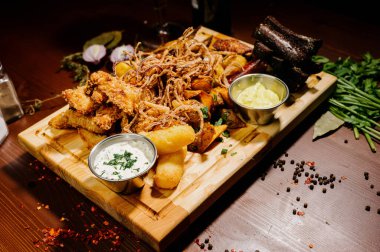 Bira ve abur cubur seçimi. Cips, balık, bira sosu. Masanın üzerinde soslu, koyu arkaplanda bir sürü farklı bira aperatifi.