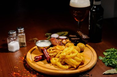 Bira ve abur cubur seçimi. Cips, balık, bira sosu. Masanın üzerinde soslu, koyu arkaplanda bir sürü farklı bira aperatifi.