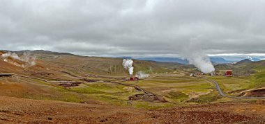 Arkasında dağlar, bir göl ve bir yol olan jeotermal enerji santralinin panoramik görüntüsü