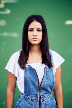 Beyaz bluz ve yeşil arka planda şort giyen uzun saçlı esmer bir kadın.