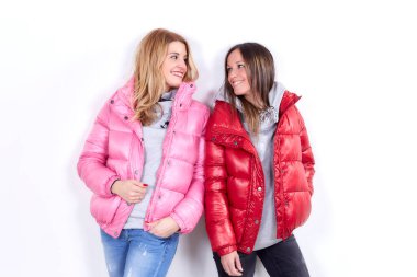 Çekici, uzun saçlı sarışın mankenler stüdyoda kuş tüyü ceketler giyiyor, birbirinize bakıyor ve beyaz bir duvara yaslanırken gülümsüyorsunuz.