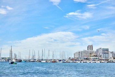 Ibiza 'da deniz manzarası, limanda yatlar ve tekneler, apartmanlar, güneşli bir yaz gününde mavi gökyüzü ve martılar..