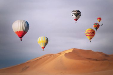 Günbatımında kum tepelerinde uçan renkli sıcak hava balonları.