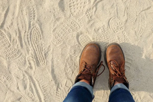 View from above to a pair of hiking trendy brown boots with shoelaces on sandy gritty background. Teenage and youth trendy casual shoes. Ready to journey! Travel activities concept. Hiking adventure.