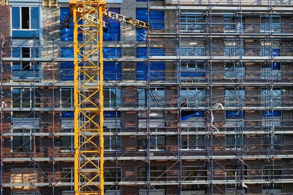 Skyscraper construction process. Facade of new commercial property for sale with yellow crane construction equipment.Assembly lines and scaffolding covering facade of residential building.