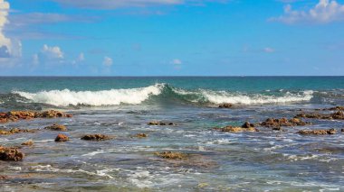 Mercan oluşumlu sığ su sahili manzarası ve Mauritius adasında hafif turkuaz dalgası. Mercanlar, köpükler ve dalgalarla dolu vahşi bir sahil..