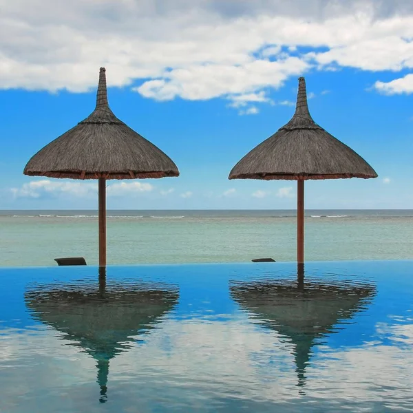 夏日里 海滩上的遮阳伞映照在热带度假胜地的无限大游泳池里 可以俯瞰平静的大海 全球大流行病造成的旅游季节危机 — 图库照片