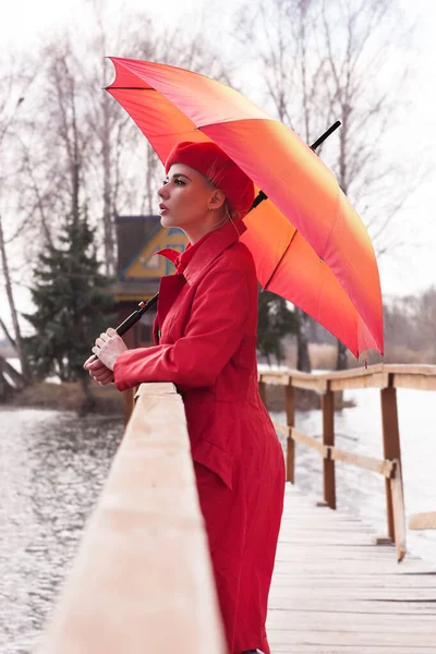 Young woman with an umbrella stands on a bridge near the river on a cloudy day