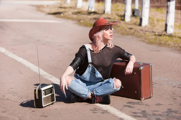 Young traveling woman with a suitcase hitchhiking on the road